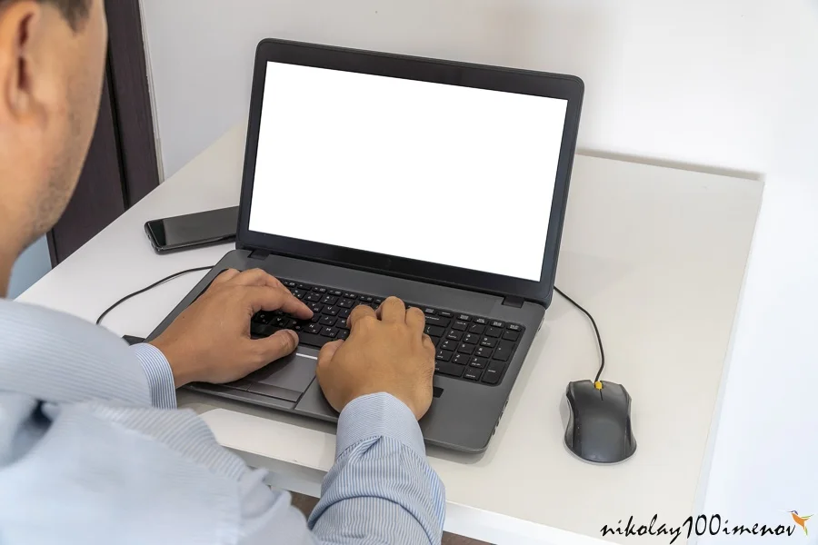 Person working on a laptop in a business office enviroment. Over the shoulder shot of man typing on a computer with blank screen.
