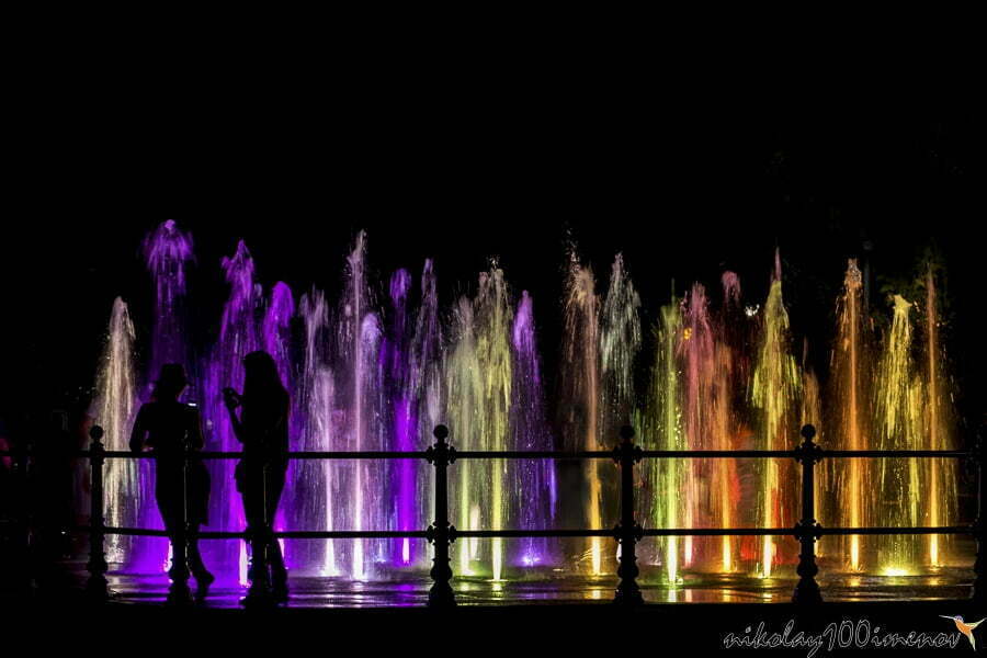 Silhouette of grils looking at a colorfully lit fountain